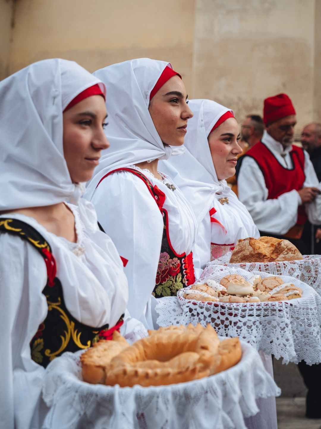 Donne indossano abiti tipici sardi e portano vassoi con dolci tradizionali